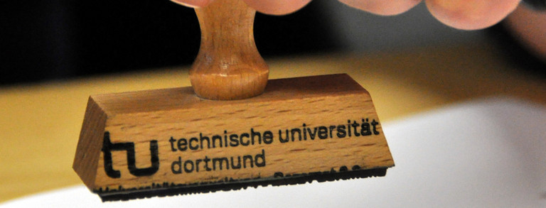 Stempel der TU Dortmund Nahufnahme eines TU Dortmund-Stempels über einem Blatt Papier